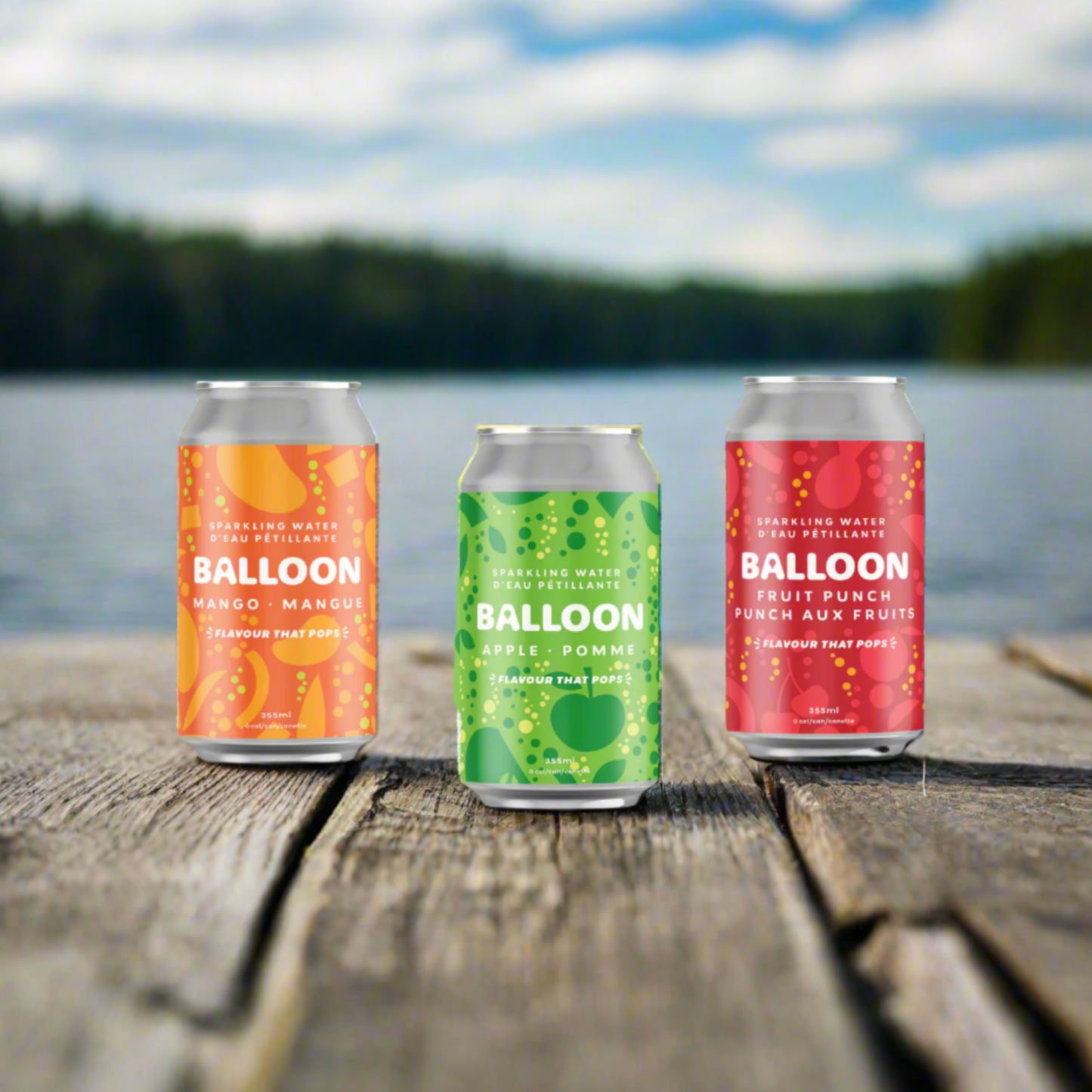 Three cans of Balloon Sparkling Water on a dock by a lake